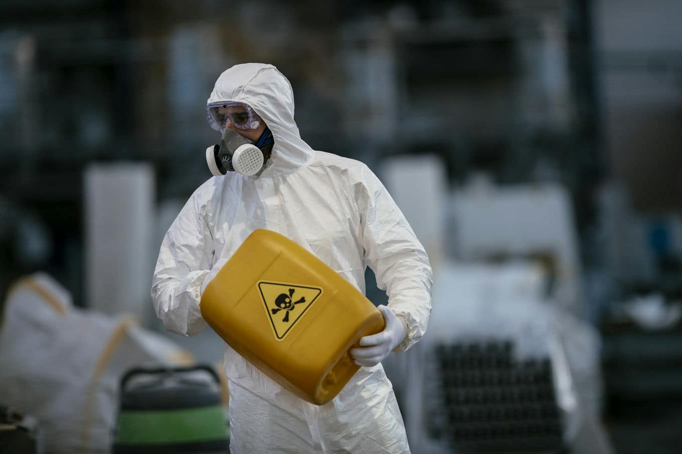 mężczyzna w kombinezonie ochronnym przenoszący zbiornik z chemikaliami